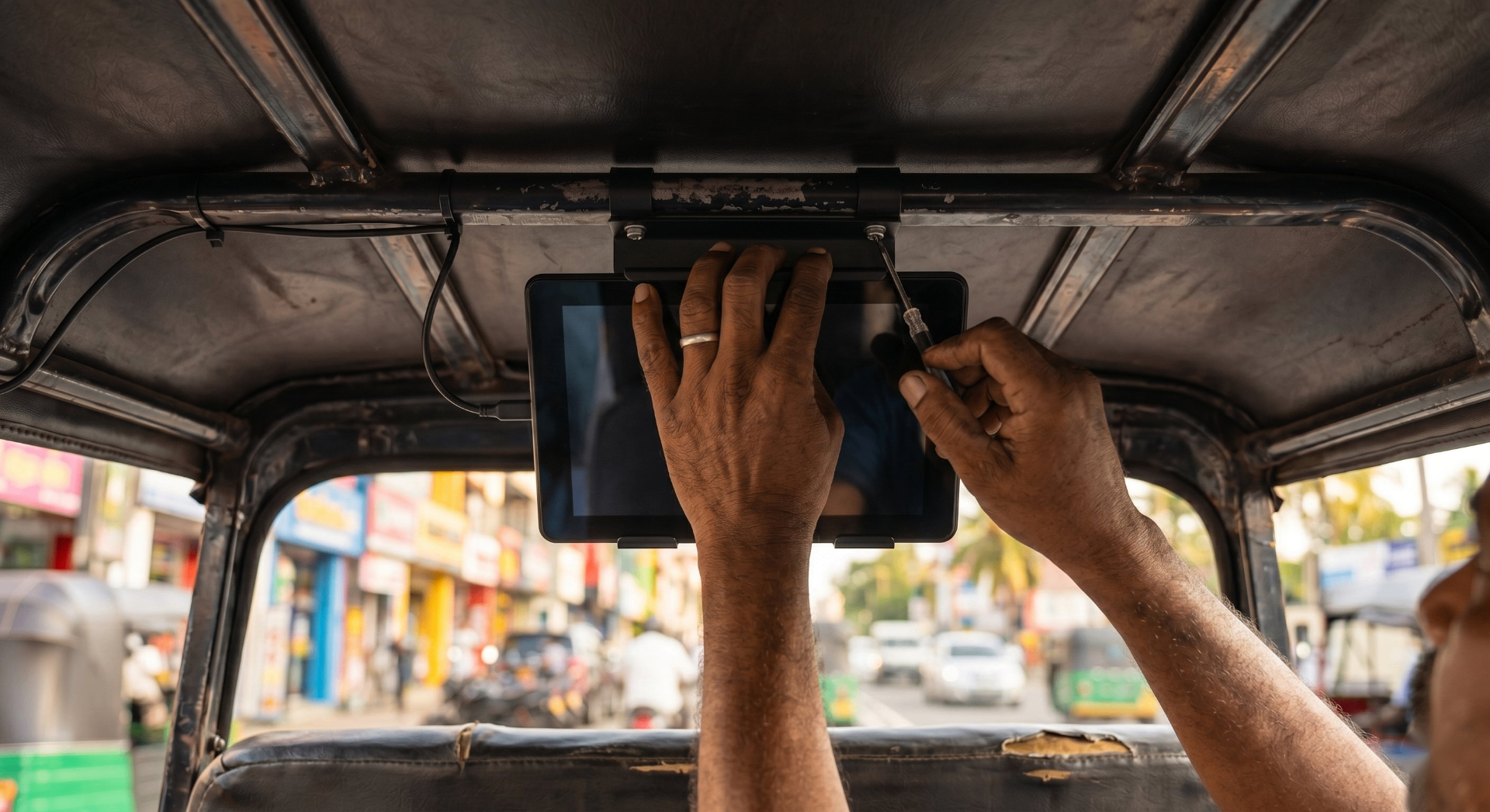 Hands fitting a tablet screen into the roof frame of a tuk-tuk on a Colombo street